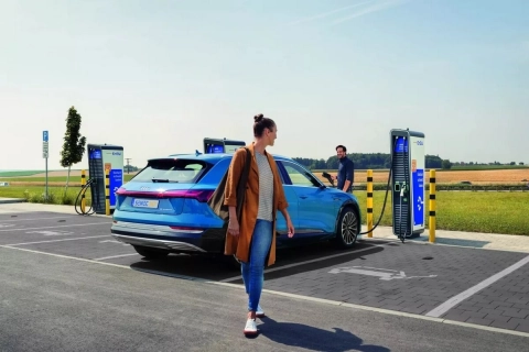 Eine junge Frau schaut sich nach ihrem neuen E-Auto um, während es mit Strom beladen wird.